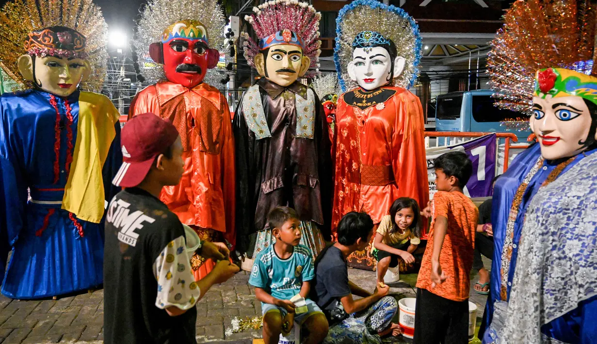 Foto pada 10 April 2019, anak-anak beristirahat dari mencari nafkah dengan mengamen ondel-ondel di jalan-jalan Jakarta. Seiring berjalan waktu, ondel-ondel yang dahulu sebagai ikon kesenian Betawi kini mudah ditemui di sejumlah jalan dan gang-gang di antara permukiman warga. (GOH CHAI HIN / AFP)