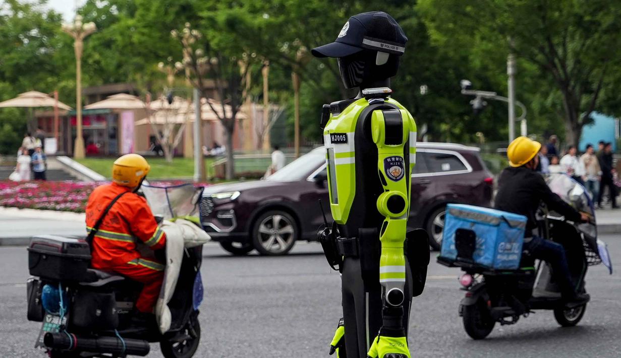 Robot-robot humanoid ini ditempatkan di persimpangan jalan utama dan area strategis, termasuk di sekitar kawasan wisata. Tampak dalam foto, orang-orang berkendara melewati robot polisi humanoid di Hangzhou, provinsi Zhejiang Timur, Tiongkok pada Minggu 3 Mei 2026. (Agatha CANTRILL/AFP)
