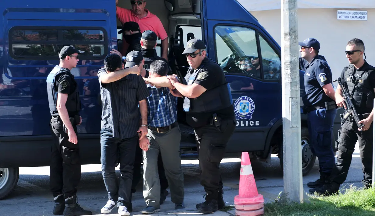 Polisi mengawal dua dari 8 perwira militer pendukung kudeta Turki, di kota Alexandroupoli, Minggu (17/7). 8 pria yang terbang dengan helikopter militer Turki itu ditahan petugas keamanan Yunani karena masuk secara ilegal. (Sakis MITROLIDIS/AFP)