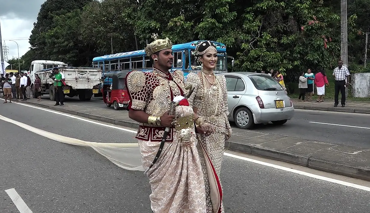 Sepasang pengantin Sri Lanka berjalan menyusuri jalan utama di pusat kota Kandy, 22 September 2017. Pasangan itu membuat kontroversi karena menggunakan sekitar 250 siswa untuk memegang saree atau gaun pengantin wanita India selama pernikahan. (STR/AFP)