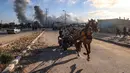Gumpalan asap hitam membumbung tinggi selama serangan Israel ketika warga Palestina yang mengendarai gerobak yang ditarik kuda melaju di sepanjang jalan Salah al-Din di dekat kamp pengungsi Nusseirat, Jalur Gaza Tengah, pada 25 Juni 2025. (Eyad BABA/AFP)