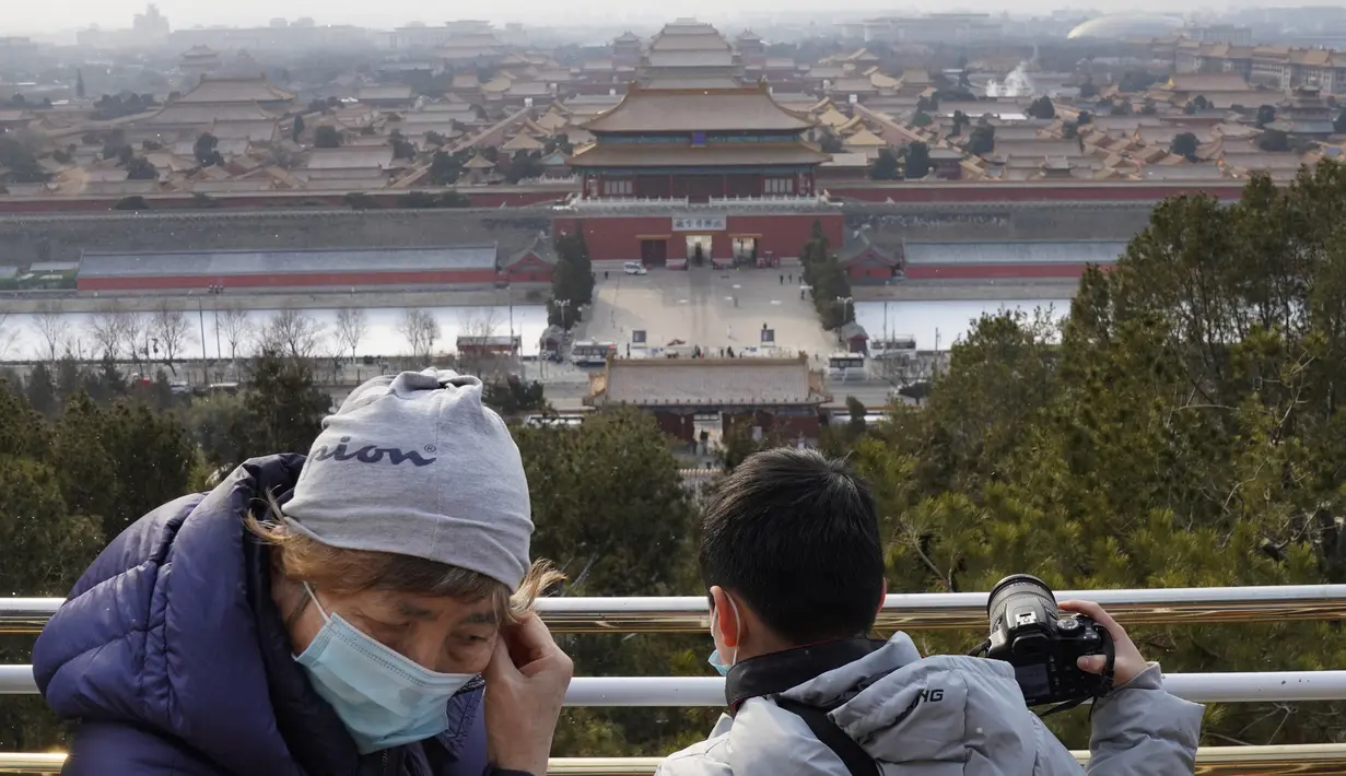 Seorang lansia mengenakan masker di dekat pemandangan menghadap Kota Terlarang dari taman Jingshan pada hari bersalju di Beijing, China, Selasa (19/1/2021). China kini berurusan dengan pandemi corona di timur lautnya yang mendorong penguncian ketat dan pembatasan perjalanan. (AP Photo/Ng Han Guan)