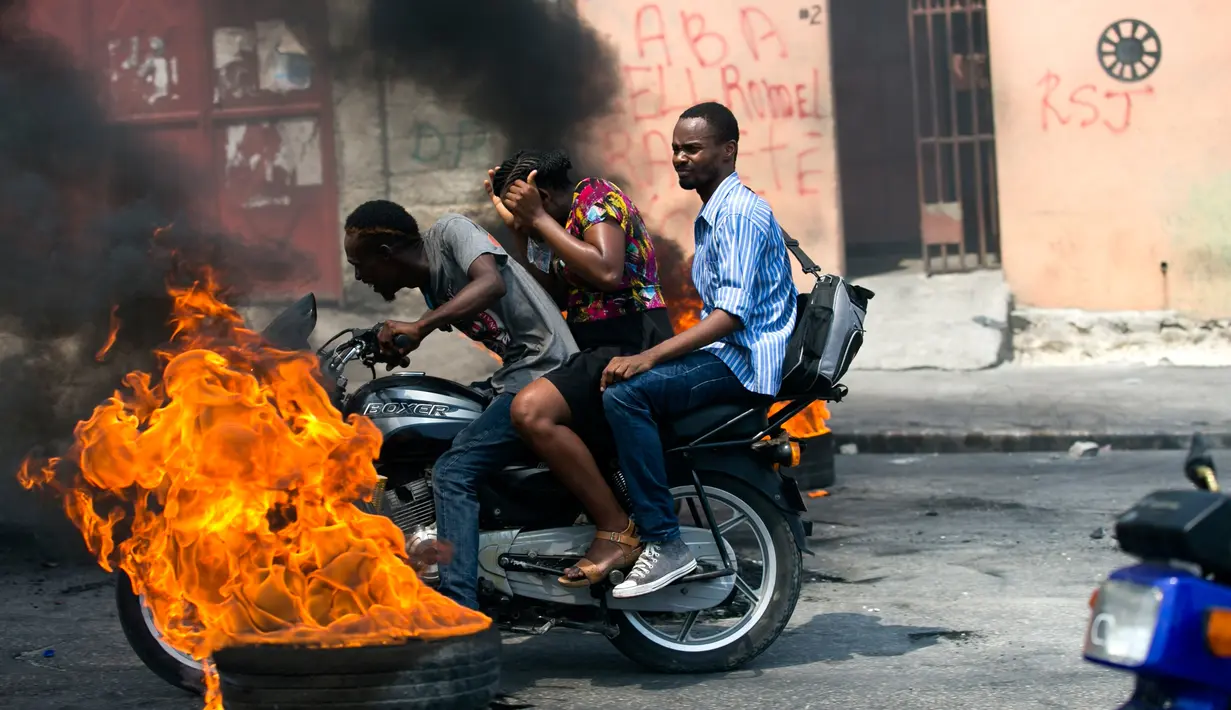 Pengendara sepeda motor melewati barikade ban yang terbakar saat terjadi protes krisis bahan bakar di Port-au-Prince, Haiti, Senin (16/9/2019). Krisis bahan bakar menyebabkan transportasi umum tidak beroperasi. (AP Photo/Dieu Nalio Chery)