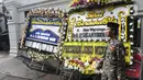 Warga berdiri dekat karangan bunga ucapan duka cita atas meninggalnya KH Salahuddin Wahid atau Gus Sholah di kawasan Mampang Prapatan, Jakarta, Senin (3/2/2020). Gus Sholah akan dimakamkan di kompleks pemakaman keluarga di dalam kawasan Pesantren Tebuireng, Jawa Timur. (Liputan6.com/Herman Zakharia)
