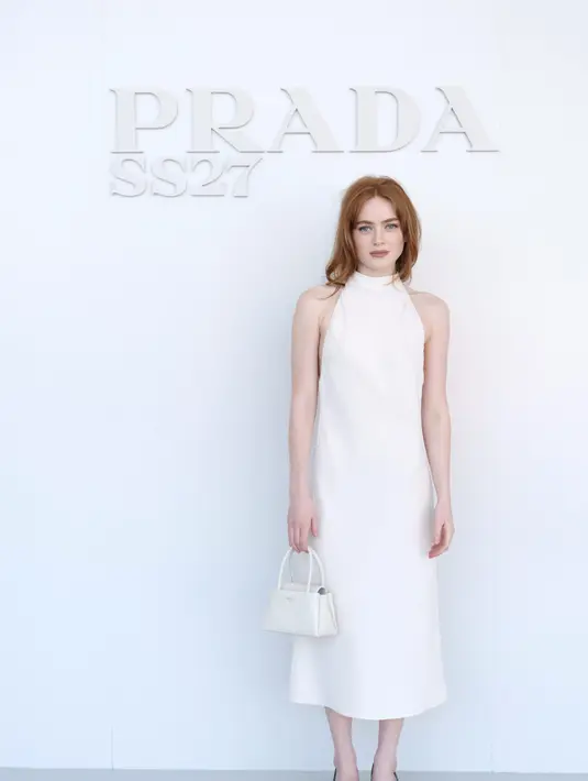 Sadie Sink mengenakan dress halter midi putih, dipadukan tas Prada putih dan heels runcing hitam bertali metalik [dok. Prada]
