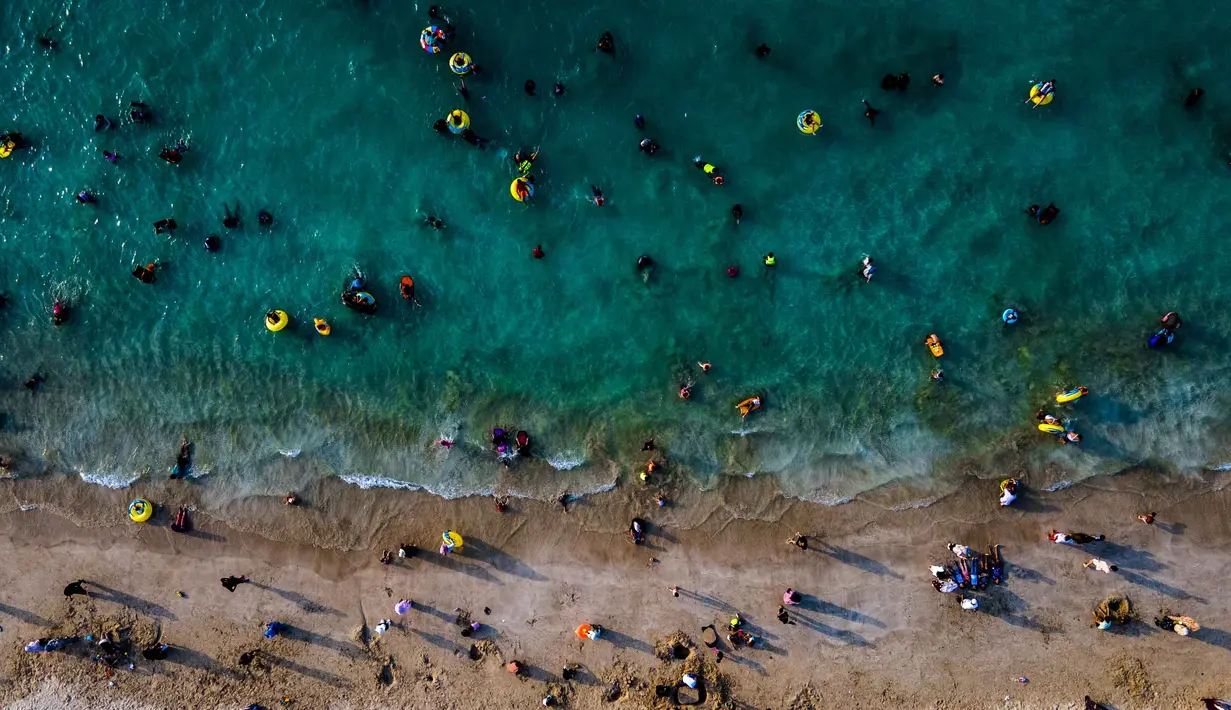 Terletak di Aceh Besar, Pantai Lhoknga, merupakan salah satu destinasi wisata paling menakjubkan di Indonesia. Tampak foto udara menunjukkan orang-orang saat berkumpul menikmati masa libur panjang Idulfitri di area olahraga air, Pantai Lhoknga, Aceh, pada Kamis 26 Maret 2026. (Chaideer MAHYUDDIN/AFP)
