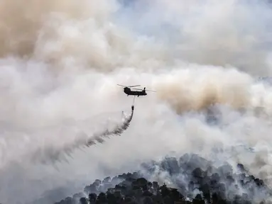 Sebuah helikopter militer menjatuhkan air di atas hutan dekat Desa Schinos, Korintus, Yunani, Kamis (20/5/2021). Kebakaran hutan besar di sebelah barat Athena merusak rumah-rumah dan mendorong evakuasi. (AP Photo/Petros Giannakouris)