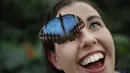 Kupu-kupu besar, Blue Morpho menghinggapi wajah Anna Platoni saat pembukaan, "Butterflies in the Glasshouse", di RHS Wisley di Wisley, Inggris, (13/1). Butterflies in the Glasshouse adalah rumah kaca untuk menjaga habitat kupu-kupu. (AFP/Adrian Dennis)