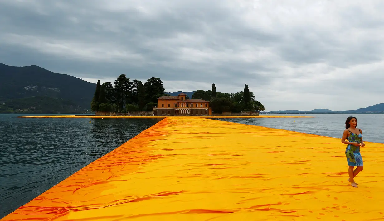 Seorang wanita berjalan diatas instalasi seni 'The Floating Piers' buatan seniman kelahiran Bulgaria Christo Vladimirov Yavachev atau dikenal sebagai Christo , di Danau Iseo , Italia utara , (16/6). (REUTERS / Stefano Rellandini)