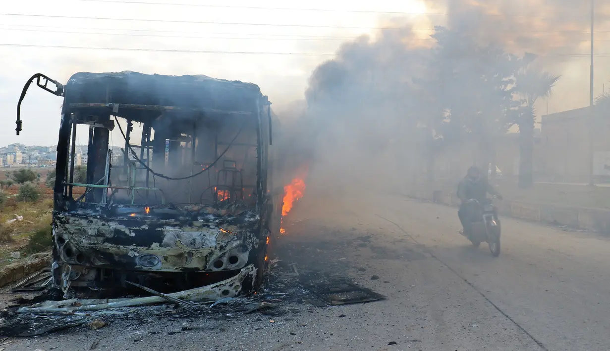 Pengendara motor melewati bus yang diserang dan dibakar saat dalam perjalanan ke al-Foua dan Kefraya di dekat Idlib, Suriah, Minggu (18/12). Bus itu sedianya untuk mengevakuasi warga yang sakit dan terluka di Aleppo timur. (REUTERS/Ammar Abdullah)