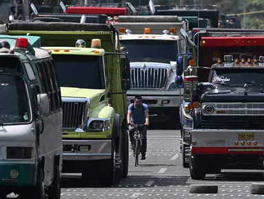 Seorang pria mengendarai sepedanya di jalan yang diblokir oleh pengemudi truk selama protes di Bogota, Kolombia, Selasa (3/9/2024). (Raul ARBOLEDA / AFP)