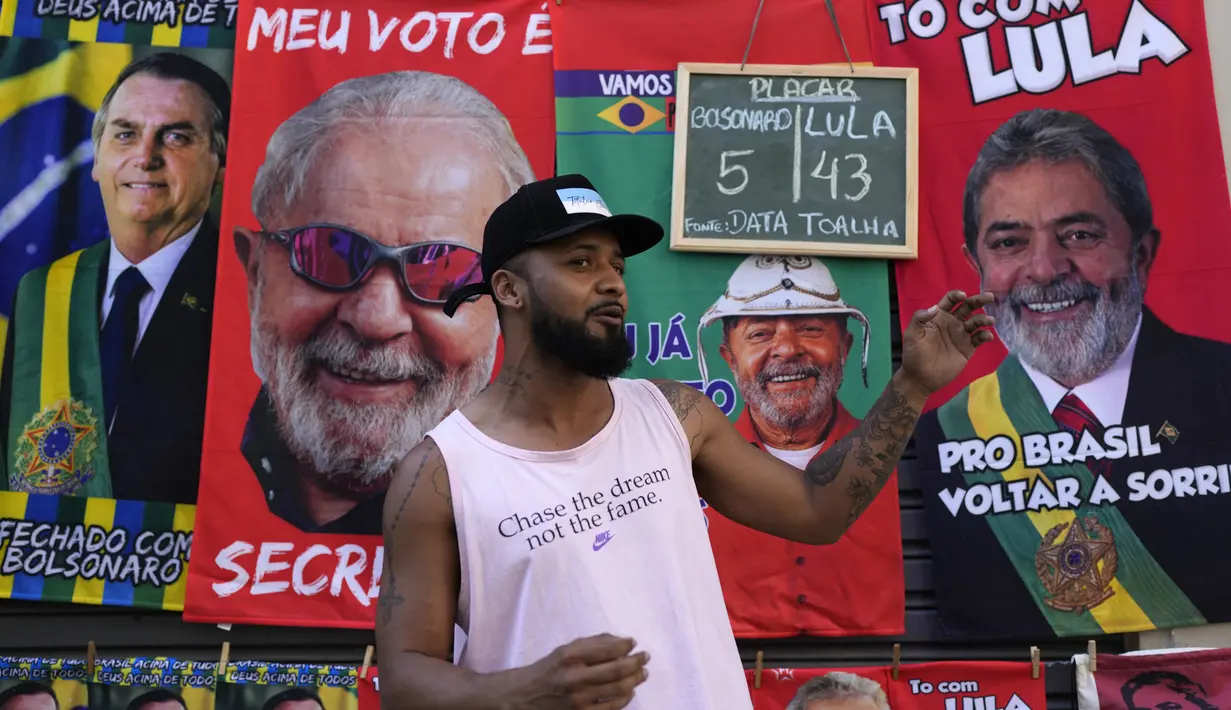 Jose Lucas da Silva berdiri di depan handuk bergambar Presiden Brasil Jair Bolsonaro (kiri) dan mantan Presiden Brasil Luiz Inacio da Silva atau Lula yang dia jual menjelang pemilihan umum presiden di Rio de Janeiro, Brasil, 27 Juli 2022. Ada dua calon yang diunggulkan pada pemilihan umum presiden di Brasil. (AP Photo/Silvia Izquierdo)