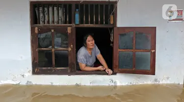Warga melihat keluar jendela saat banjir di RW 07, Kelurahan Pekayon, Jakarta Timur, Sabtu (20/2/2021). Banjir di kawasan tersebut terjadi akibat curah hujan yang tinggi. (Liputan6.com/Herman Zakharia)