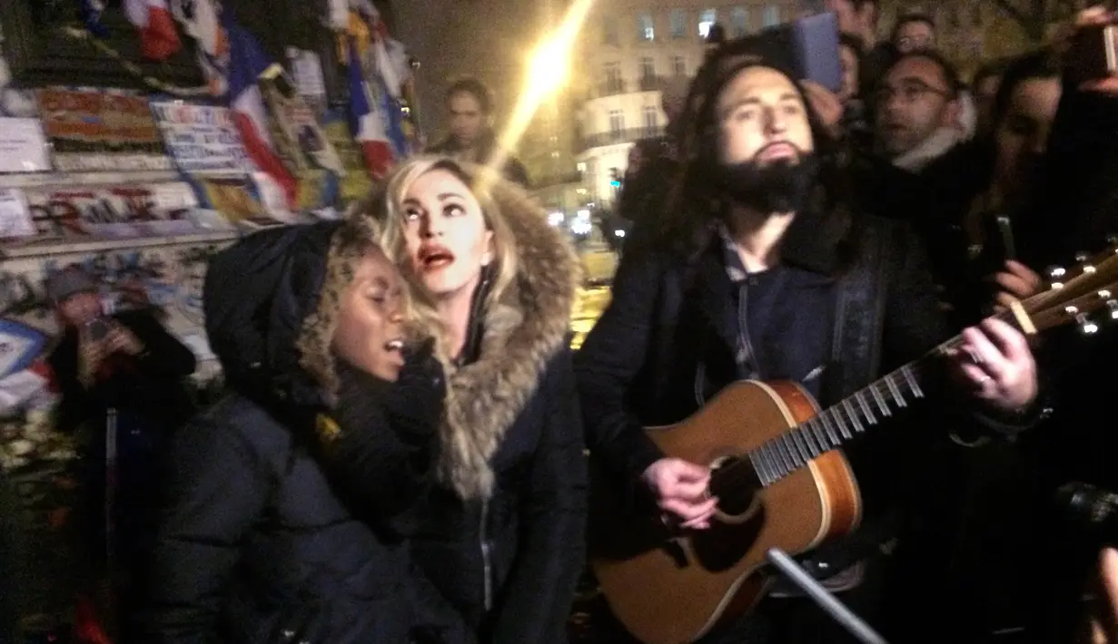 Penyanyi Madonna dan putranya David Banda diiringi gitaris Monte Pittman menggelar konser jalanan di Place de la Republique, dekat tempat peringatan para korban serangan 13 November Paris yang menewaskan 130 orang, Kamis (10/12/2015). (JULES MAHE/AFP)