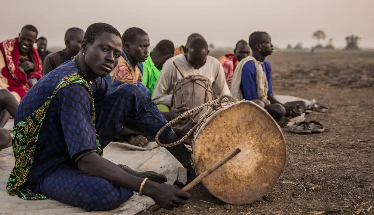 Penggembala dari suku Dinka bermain alat musik di kamp ternak mereka di Mingkaman, Lakes State, Sudan Selatan, Minggu (4/3). Mereka akan mendirikan kamp ternak besar untuk memastikan hewan mereka dekat dengan air. (Stefanie GLINSKI/AFP)