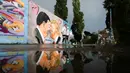 Orang-orang berjalan di depan Graffiti yang menggambarkan Presiden AS Trump (kanan) dan Presiden Tiongkok Xi Jinping saling berciuman dengan mengenakan masker di tembok taman umum Mauerpark di Berlin, Jerman, Rabu, (29/4/2020). (AP/Markus Schreiber)