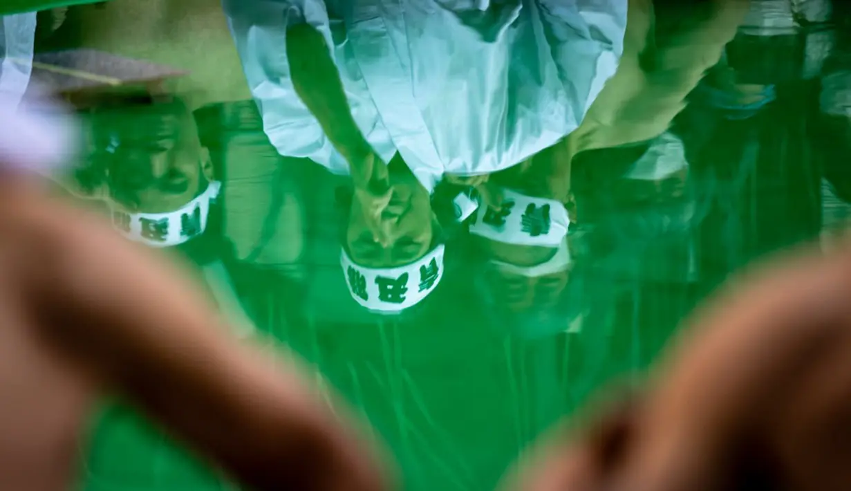 Refleksi pada air memperlihatkan penganut Shinto melakukan pemanasan sebelum mandi dengan air dingin di Kuil Teppozu Inari, Tokyo, Jepang, 8 Januari 2023. Ritual Tahun Baru ini dilakukan untuk memurnikan jiwa dan raga. (Philip FONG/AFP)