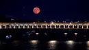 Foto yang diambil di Paris pada 3 Juli 2023 ini menunjukkan supermoon Juli, yang dikenal sebagai Buck Moon, dengan 'Pont de Bercy' di latar depan.
(Stefano RELLANDINI / AFP)