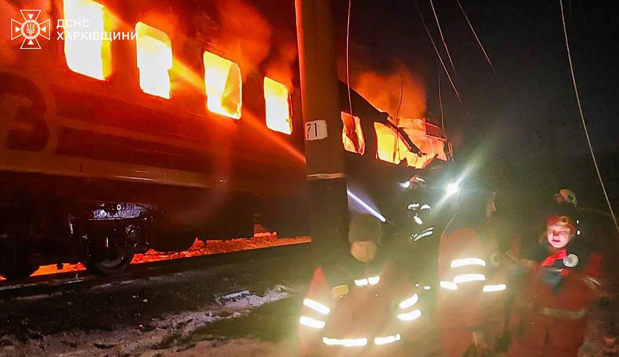 Menurut keterangan otoritas Ukraina, serangan ini menewaskan sedikitnya empat orang dan melukai dua lainnya. Tampak dalam foto yang diberikan dan dirilis oleh Layanan Darurat Ukraina pada 27 Januari 2026 ini, petugas medis Ukraina berdiri di samping gerbong kereta yang terbakar setelah serangan udara di lokasi yang tidak diungkapkan di wilayah Kharkiv, di tengah invasi Rusia ke Ukraina. (Handout/UKRAINIAN EMERGENCY SERVICE/AFP)
