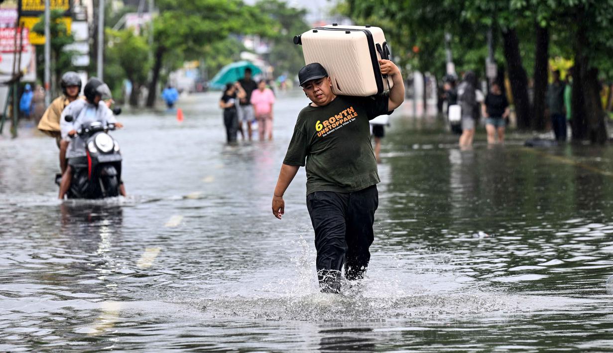 Ketinggian air akibat banjir mencapai sekitar 60 cm. Tampak dalam foto, seorang tamu hotel membawa kopernya sambil menerobos air di jalan yang tergenang banjir akibat hujan lebat di Legian Kuta, Denpasar, Bali, pada Selasa 24 Februari 2026. (SONNY TUMBELAKA/AFP)