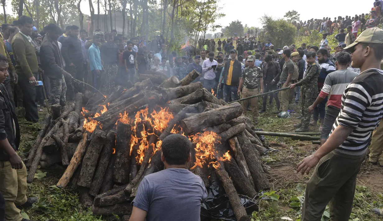 Polisi dan pekerja kehutanan bersama penduduk desa menyaksikan tubuh gajah dibakar setelah kereta penumpang melaju menabrak dua gajah yang melintasi rel di desa Batasi dekat perbatasan India-Nepal, sekitar 37 km dari Siliguri (11/12/2019). (AFP/Diptendu Dutta)