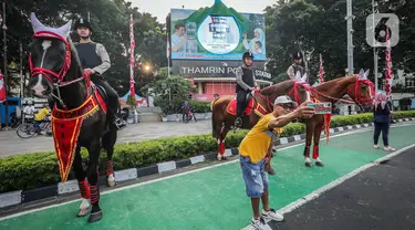 Warga berswafoto dengan polisi berkuda yang bersiaga saat hari bebas kendaraan bermotor (HBKB) atau car free day (CFD) di kawasan Bundaran HI, Jakarta, Minggu (23/7/2023). Selain bagian dari pengamanan, kehadiran polisi berkuda ini juga menjadi sarana wisata yang menghibur warga saat beraktivitas di CFD. (Liputan6.com/Faizal Fanani)
