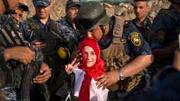 Seorang anggota polisi Federal Irak  mencium seorang anak perempuan saat merayakan keberhasilan mereka menyingkirkan militan ISIS dari Kota Tua Mosul, Minggu (9/7). ISIS merebut Mosul pada musim panas 2014. (FADEL SENNA/AFP)