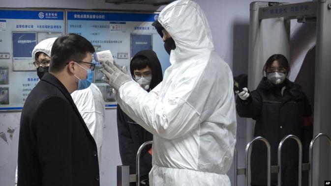 Petugas yang memakai pakaian pelindung memeriksa suhu badan seorang penumpang kereta bawah tanah di Beijing, Minggu (26/1). (Source: AP)