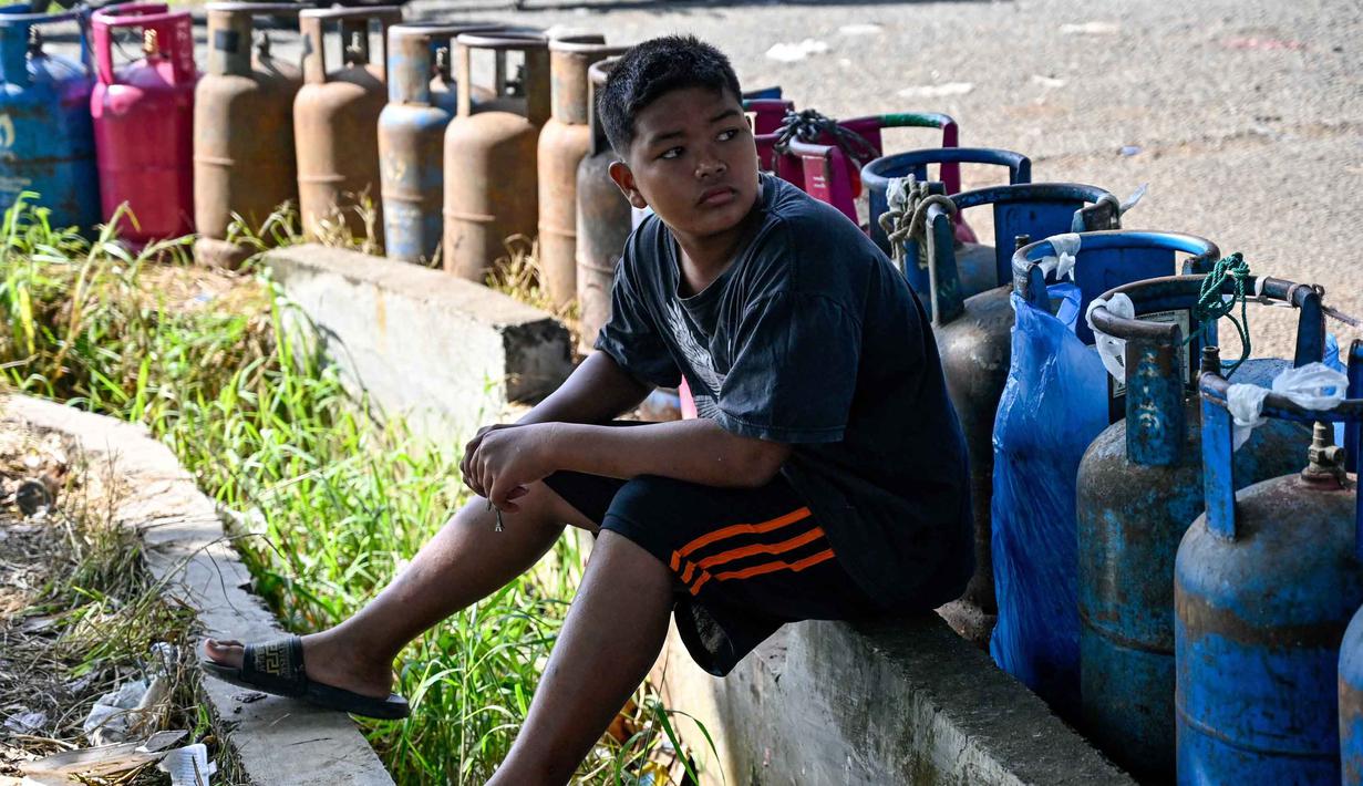 Warga berharap Pemerintah Kota Banda Aceh segera berkoordinasi dengan pihak terkait, termasuk Pertamina dan agen distribusi, untuk memastikan pasokan gas kembali normal. Tampak dalam foto, seorang anak laki-laki menunggu untuk membeli tabung gas di sebuah stasiun pengisian dan pembelian LPG setelah banjir bandang di Banda Aceh pada Rabu 17 Desember 2025. (CHAIDEER MAHYUDDIN/AFP)