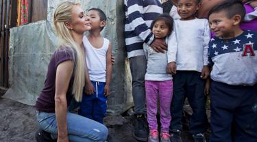 Aktris Paris Hilton dicium seorang anak saat mengunjungi keluarga yang terkena dampak gempa bumi pada September 2017 di San Gregorio Atlapulco, Meksiko (12/11). Paris Hilton tampil mengenakan kaos, jeans dan sepatu hitam. (AFP Photo/Antonio Nava)