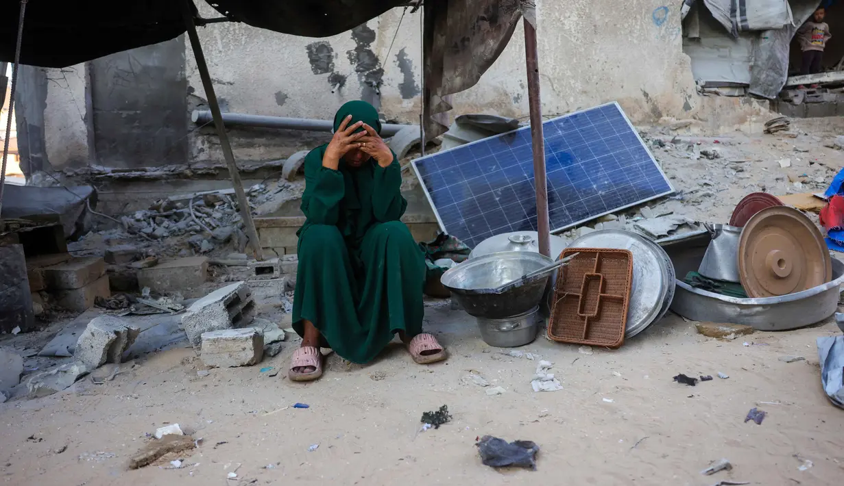 Seorang perempuan bereaksi sambil duduk di samping peralatan makannya yang diselamatkan dari reruntuhan rumah yang hancur akibat serangan Israel di Khan Younis, Jalur Gaza selatan, pada Rabu 29 Oktober 2025. Kesepakatan gencatan senjata yang dimotori Amerika Serikat dan mulai berlaku pada 10 Oktober lalu terancam gagal, kedua pihak bertikai baik Israel maupun Hamas sama-sama saling menuduh satu sama lain melanggar. (BASHAR TALEB/AFP)