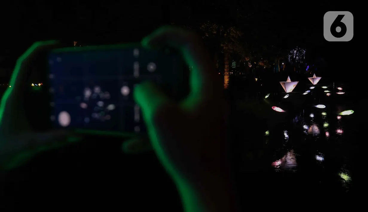 Warga saat memotret Jakarta Lights Festival di Taman Sumenep, Jakarta, Jumat (23/12/2022). Pemprov DKI Jakarta menggelar acara Jakarta Lights Festival sebagai rangkaian perayaan Natal dan Tahun Baru (Nataru) 2023. (Liputan6.com/Herman Zakharia)