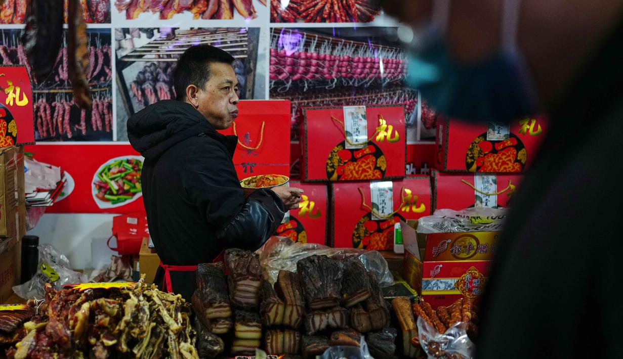 Untuk diketahui, perayaan Tahun Baru Imlek 2577 Kongzili jatuh pada Selasa 17 Februari 2026. Tampak dalam foto, seorang pedagang menikmati makanannya di lapaknya sementara orang-orang berbelanja saat bazar menyambut Tahun Baru Imlek di Beijing, China, Minggu 1 Februari 2026. (AP Photo/Andy Wong)