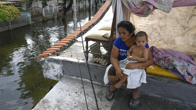 Seorang wanita dan anaknya duduk di atap rumah mereka yang terendam banjir di Mata Redonda, Maracay, Venezuela, Rabu (21/10/2020). Lusinan keluarga mencari perlindungan di atap rumah mereka untuk melindungi barang pribadi mereka. (AP Photo/Matias Delacroix)