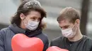 Pasangan yang mengenakan masker memegang balon berbentuk hati saat berjalan di Kiev, Ukraina, 1 April 2020. Organisasi Kesehatan Dunia (WHO) mengumumkan virus corona COVID-19 sebagai pandemi sejak 11 Maret 2020 lalu. (Sergei SUPINSKY/AFP)