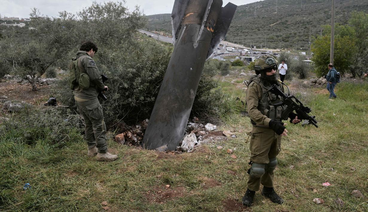 Beberapa personel pasukan keamanan Israel berada di lokasi untuk menjaga sisa-sisa proyektil rudal Iran yang tertancap di tanah. Tampak dalam foto, personel militer Israel mengamankan lokasi jatuhnya puing-puing rudal Iran di desa Kifl Haris, Tepi Barat, Selasa, 24 Maret 2026. (AP Photo/Majdi Mohammed)