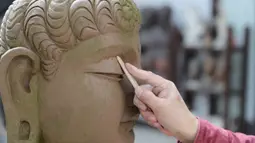 Seniman Du Yongwei menyempurnakan detail sebuah model dari tanah liat sebelum mewarnainya di Dunhuang, Provinsi Gansu, China, Minggu (5/4/2020). Keterampilan seni mewarnai patung masuk dalam daftar warisan budaya tingkat provinsi di Gansu. (Xinhua/Du Zheyu)