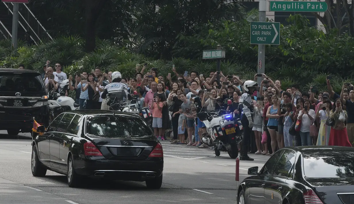 Kerumunan orang menyaksikan iring-iringan mobil yang diyakini membawa pemimpin Korea Utara Kim Jong-un di Orchard Road menuju St Regis Hotel, Singapura, Minggu (10/6). Kedatangan Kim menjelang pertemuan bersejarah dengan Donald Trump. (AP/Joseph Nair)