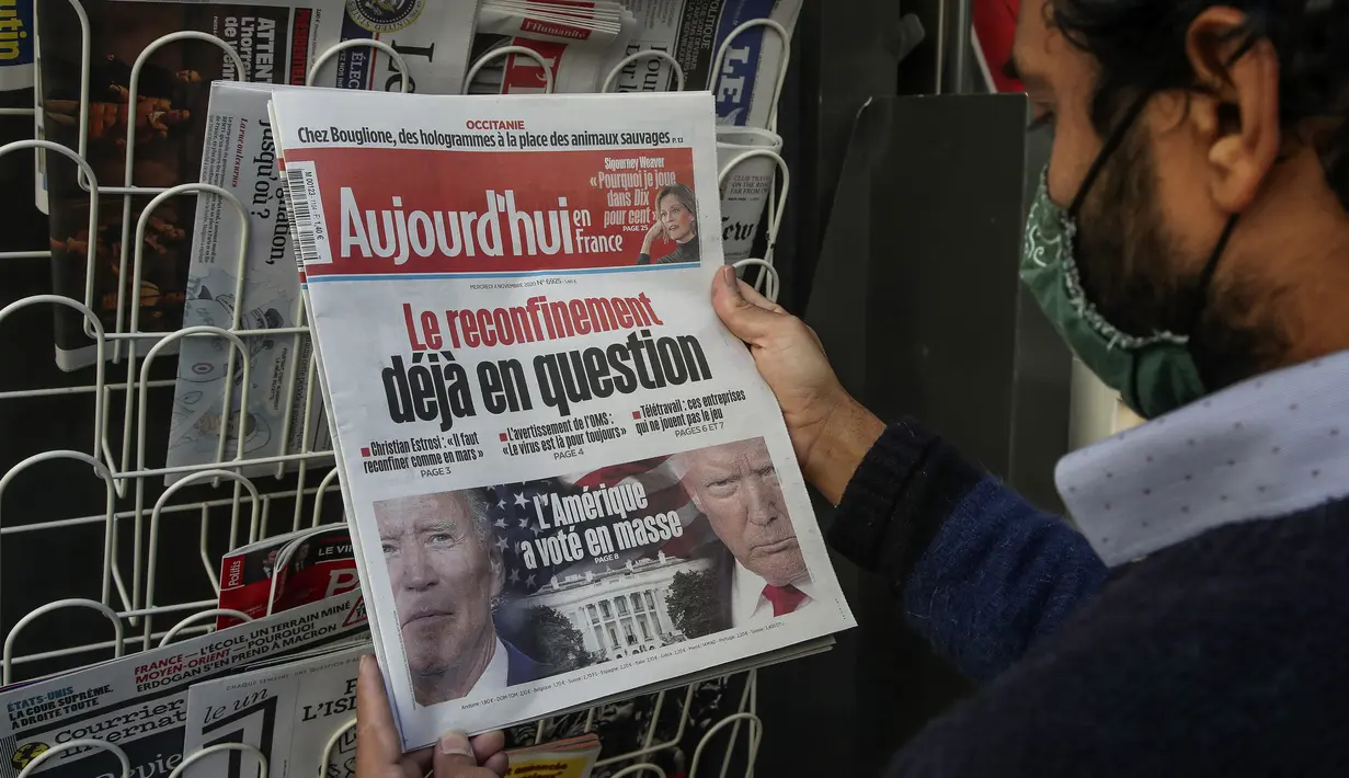 Seorang pria yang memakai masker membaca berita utama pemilihan presiden AS di stan surat kabar di Paris pada Rabu (4/11/2020). (AP Photo/Michel Euler)