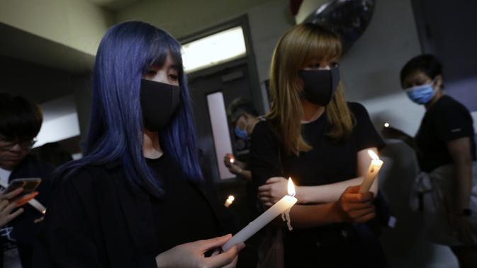 Dua wanita memegang lilin ketika mereka memberi penghormatan kepada mahasiswa Alex Chow Tsz-lok yang tewas di Hong Kong (8/11/2019). Tewasnya Chow memicu kemarahan lebih besar terhadap pihak berwenang di wilayah China semi-otonom. (AP Photo/Dita Alangkara)