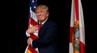 Capres AS dari Partai Republik, Donald Trump memeluk bendera AS saat melakukan kampanye menyapa pendukungnya di Tampa, Florida, AS (24/10). Trump akan bertarung dengan Hillary Clinton memperebutkan kursi di Gedung Putih. (REUTERS/Jonathan Ernst)