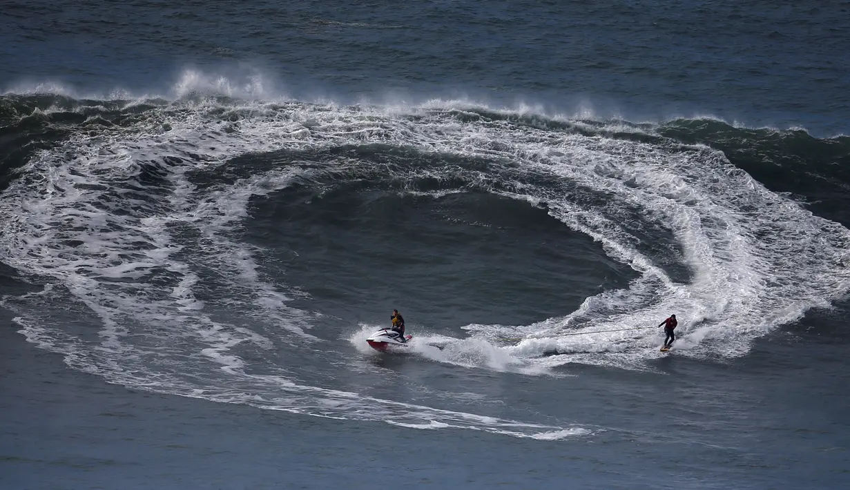 Motor boat menarik seorang peselancar saat menunggu ombak besar datang di Praia do Norte di Nazare, Portugal (19/11). Selancar merupakan sebuah olahraga yang dilakukan di atas ombak yang tinggi.  (Reuters/Rafael Marchante)