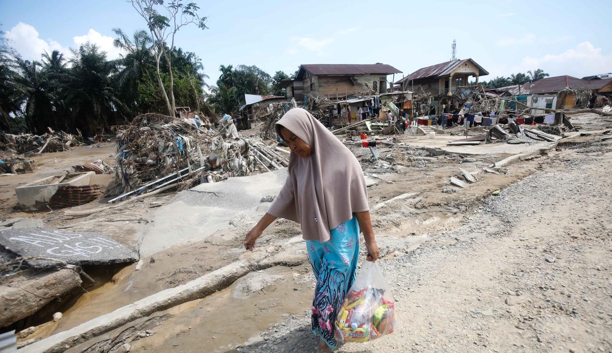 Sejumlah kendaraan roda empat teronggok dengan posisi terbalik atau tercebur ke parit. Tampak dalam foto, seorang korban membawa barang-barang bantuan di daerah yang terdampak banjir bandang di Aceh Tamiang, Sumatera, Indonesia, Jumat 5 Desember 2025. (AP Photo/Binsar Bakkara)