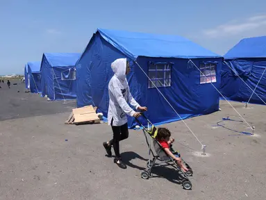Seorang perempuan Lebanon yang mengungsi mendorong kereta bayi di dekat tenda-tenda biru yang didirikan pemerintah untuk orang-orang yang meninggalkan rumah dan desa mereka di pinggiran selatan Beirut dan Lebanon Selatan, Jumat 22 Mei 2026. (Anwar AMRO/AFP)