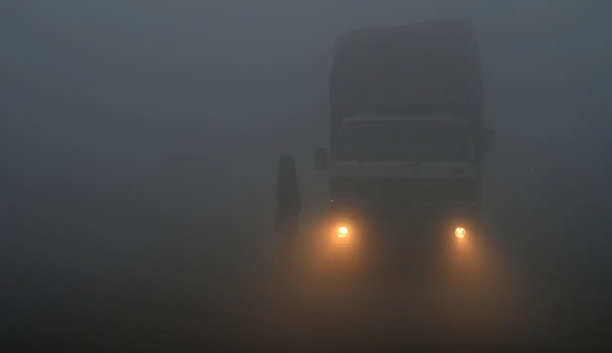 Seorang pria berdiri di samping truk di sepanjang jalan di tengah cuaca berkabut di Lahore (21/12/2022). Beberapa penerbangan dialihkan ke bandara lain akibat cuaca berkabut. (AFP/Arif Ali)