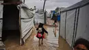 Situasi ini memperburuk kehidupan warga Gaza yang tinggal di lokasi penampungan. Tampak dalam foto, warga Palestina berjalan melewati tenda-tenda sementara yang terendam banjir setelah hujan deras di Deir al-Balah, Jalur Gaza tengah, Selasa 25 November 2025. (AP Photo/Abdel Kareem Hana)