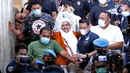 M Rizieq Shihab (tengah) mengangkat tangan saat meninggalkan gedung Ditreskrimum Polda Metro Jaya, Jakarta, Minggu dini hari (13/12/2020). Rizieq Shihab ditahan setelah menjalani pemeriksaan sebagai tersangka penghasutan dan kerumunan di tengah pandemi COVID-19. (Liputan6.com/Helmi Fithriansyah)