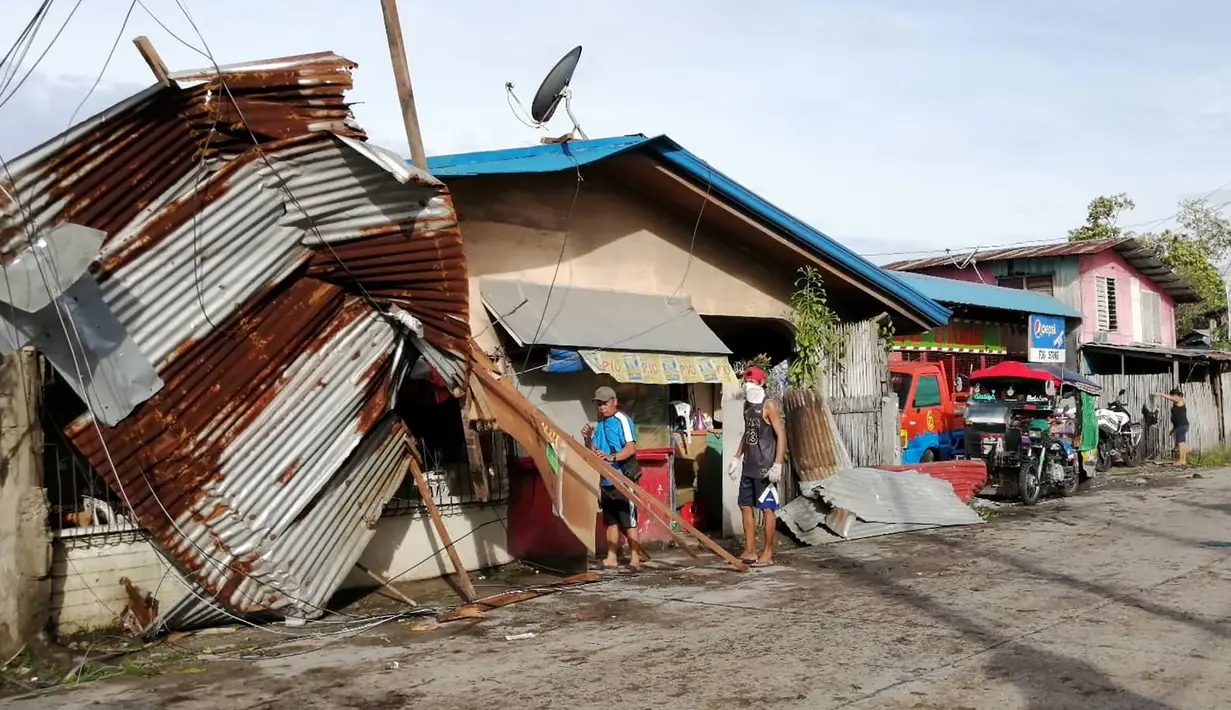 Warga berdiri dekat sebuah rumah yang rusak akibat terjangan topan Phanfone yang menerjang Ormoc City, Provinsi Leyte, Filipina, Rabu (25/12/2019). Topan membuat jutaan warga di negara yang mayoritas beragama Katolik itu merayakan Natal dengan kesedihan. (RONALD FRANK DEJON/AFP)