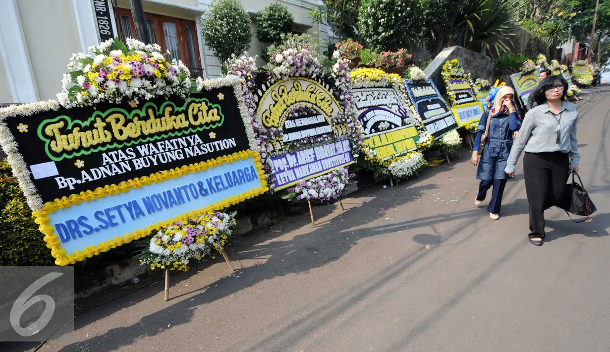 Warga melintas di depan Karangan bunga di rumah duka almarhum Adnan Buyung di kawasan Lebak Bulus, Jakarta, Rabu (23/9/2015). Adnan menghembuskan napas terakhir pada pagi tadi pukul 10.15 WIB. (Liputan6.com/Helmi Afandi)