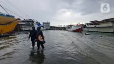Nelayan melintasi banjir rob saat cuaca ekstrem di Pelabuhan Muara Baru, Penjaringan, Jakarta Utara, Rabu (28/12/2022). Banjir ROB, hujan deras dan cuaca buruk melanda kawasan Pelabuhan Muara Baru saat siang menjelang sore hari. (Liputan6.com/Johan Tallo)
